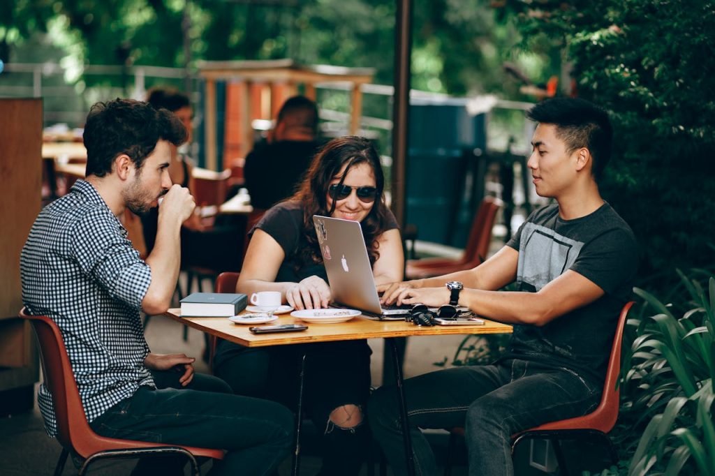 SBC Marketing London team working on a laptop at an outdoor coffee shop, enjoying teamwork and collaboration.