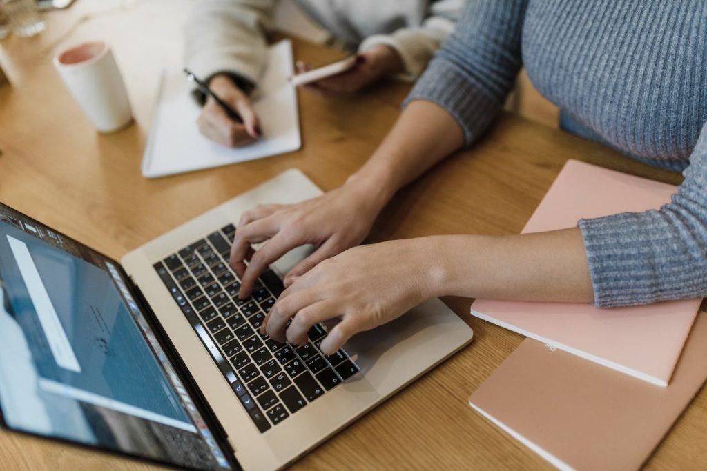 Close-up of a freelancer typing on a laptop while working remotely with coffee and notepad nearby.